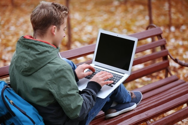 Teenager mit Laptop sitzt auf Bank im Herbstpark