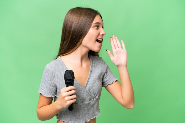 Teenager-Sängerin, die ein Mikrofon über isoliertem Hintergrund aufhebt und mit weit geöffnetem Mund zur Seite schreit