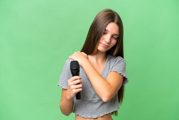 Teenager-Sängerin, die ein Mikrofon vor isoliertem Hintergrund aufnimmt und unter Schmerzen in der Schulter leidet, weil sie sich Mühe gegeben hat