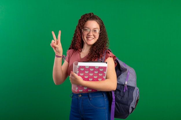 Teenager-Schüler mit Brille, Schultasche und Notizbüchern posieren auf einem Studiofoto mit grünem Hintergrund, ideal zum Zuschneiden