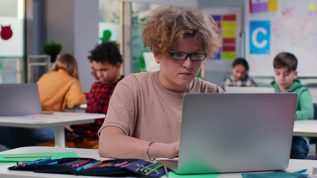 Teenager-Schüler tippt am Laptop, sitzt am Schreibtisch im Klassenzimmer