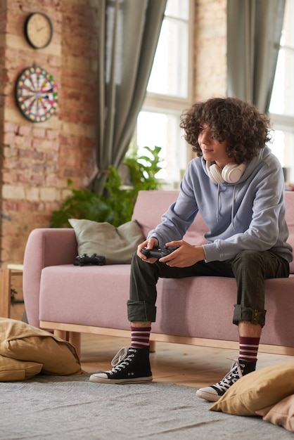 Teenager sitzen auf Sofa mit Joystick und spielen Computerspiele im Wohnzimmer
