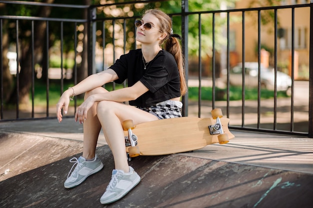 Teenager-Skatermädchen mit Skateboard sitzt auf der Rampe im Skaterpark