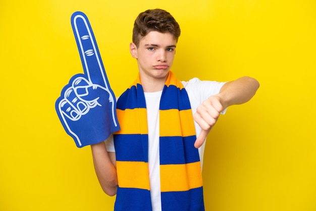 Teenager-Sportfan-Mann isoliert auf gelbem Hintergrund, der Daumen nach unten mit negativem Ausdruck zeigt