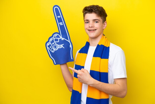 Teenager-Sportfan-Mann isoliert auf gelbem Hintergrund, der zurück zeigt