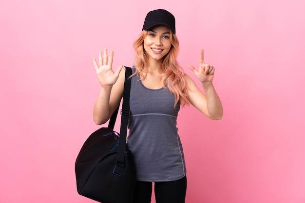 Teenager-Sportfrau mit Sporttasche über isolierter Wand, die sieben mit den Fingern zählt