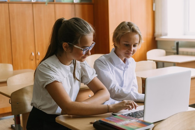 Teenager-Studenten arbeiten zusammen und schreiben in einem Heft mit einem Laptop im Klassenzimmer