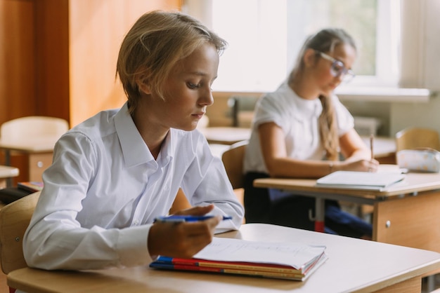 Teenager-Studenten schreiben am Schreibtisch im Klassenzimmer in ein Heft und schauen in die Kamera
