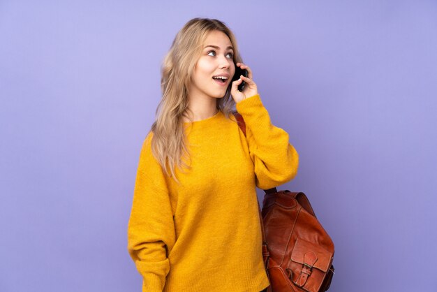 Teenager-Studentenmädchen auf lila Wand, die ein Gespräch mit dem Handy hält