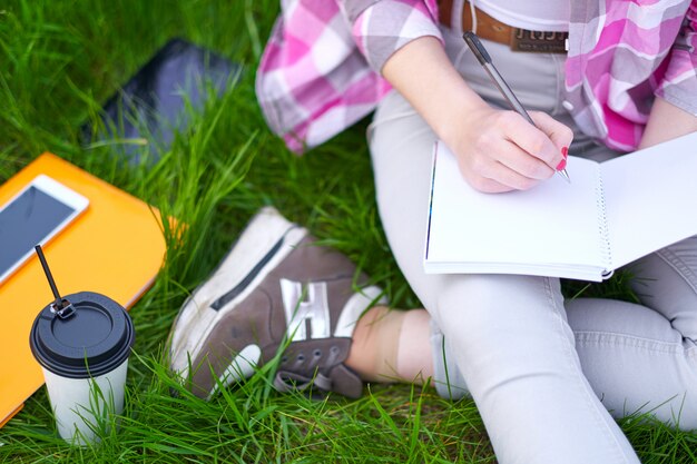 Teenager-Studentin, die im Notizbuch im Park schreibt. Vorbereitung auf Prüfungen am College oder an der Universität