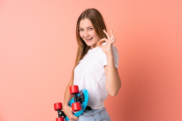 Teenager ukrainisches Skatermädchen lokalisiert auf rosa mit einem Schlittschuh und tut OK Zeichen