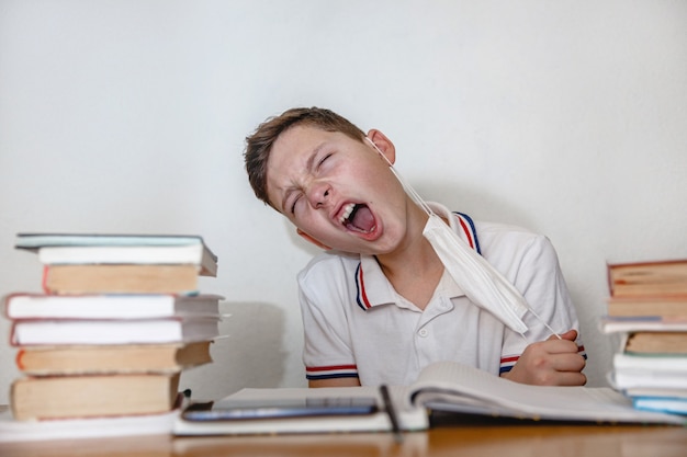 Teenager zu Hause für Lehrbücher zieht seine Maske mit einer Grimasse der Erleichterung ab