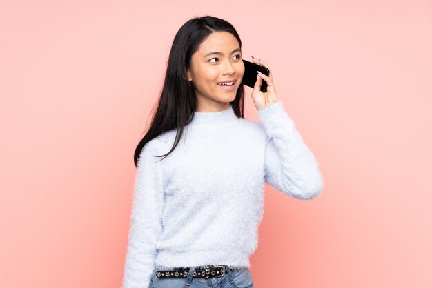 Teenagerfrau isoliert auf rosa, die ein Gespräch mit dem Handy hält