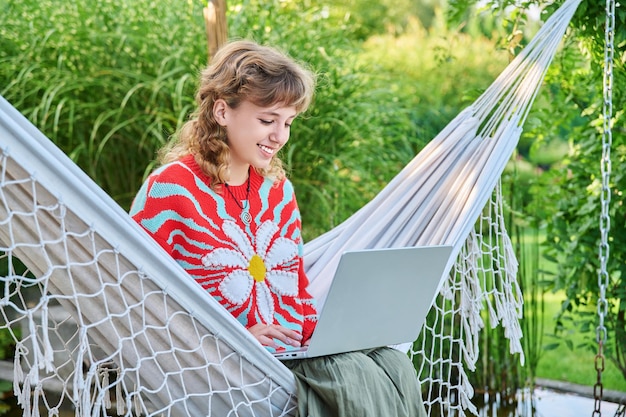 Teenagerin entspannt sich in einer Hängematte mit Laptop für Freizeitstudium Jugendliche Schüler Highschool Technologie Lebensstil Jugendkonzept
