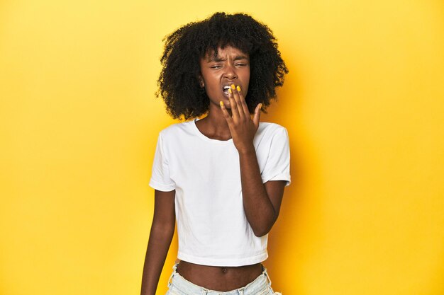 Foto teenagerin im klassischen weißen t-shirt mit gelbem studio-hintergrund gähnt und zeigt eine müde geste