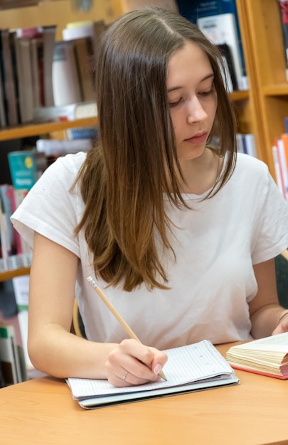 Foto teenagerin schreibt in der bibliothek auf ein buch