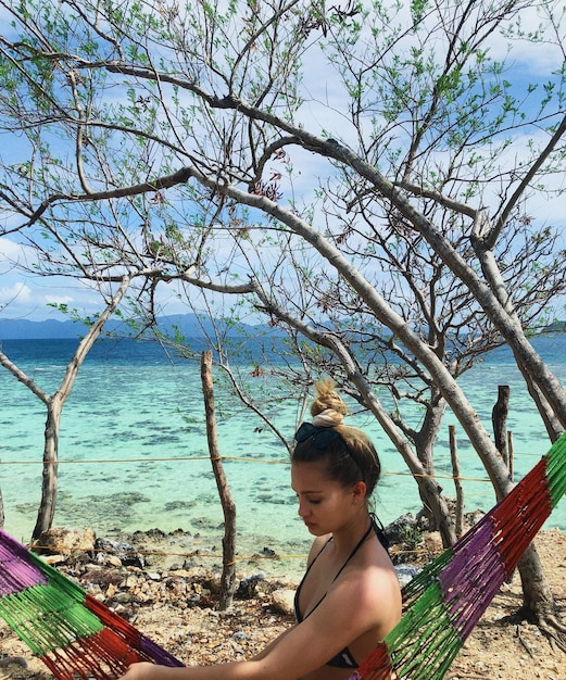 Foto teenagerin sitzt in einer hängematte am strand bei nackten bäumen