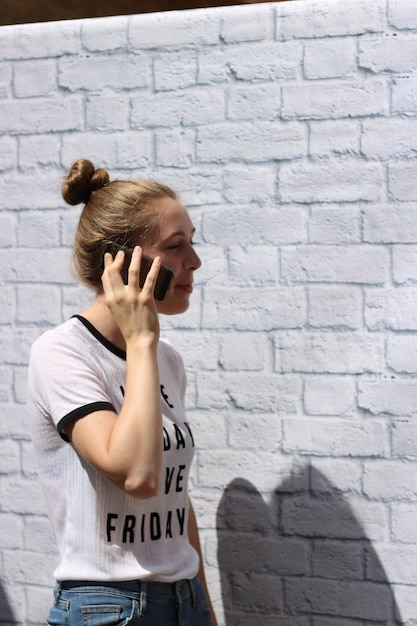 Teenagerin spricht am Handy, während sie gegen eine Backsteinmauer steht
