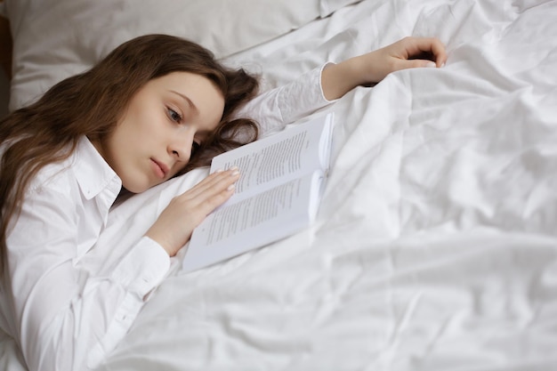 Teenagermädchen, das in ihren Träumen vom Guten neben dem Buch auf dem Bett liegt