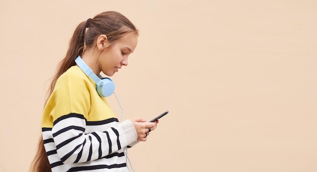 Teenagermädchen in einem Pullover benutzt ein Mobiltelefon gegen eine farbige Wand