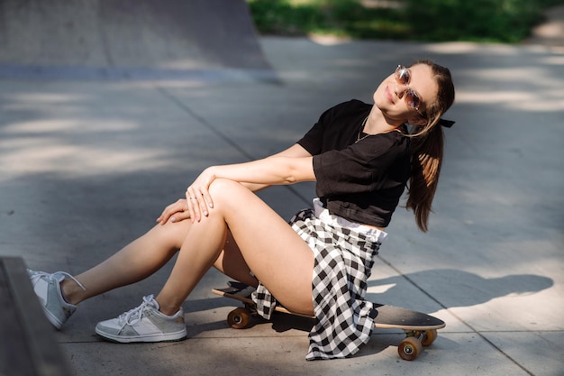 Teenagermädchen sitzt und chillt auf dem Skateboard im Skaterpark