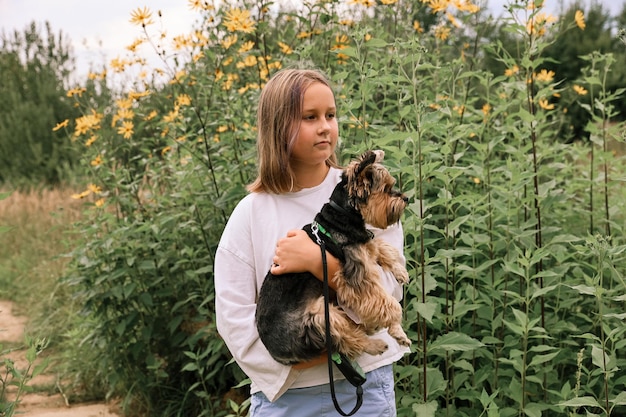 Teenie-Mädchen auf einem Spaziergang im Sommerpark mit ihrem Haustier Yorkshire-Terrier. Kind geht mit Hund spazieren