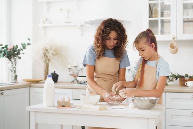 Teenie-Mädchen hilft ihrer Mutter beim Kochen von Teig in ihrer Küche zu Hause