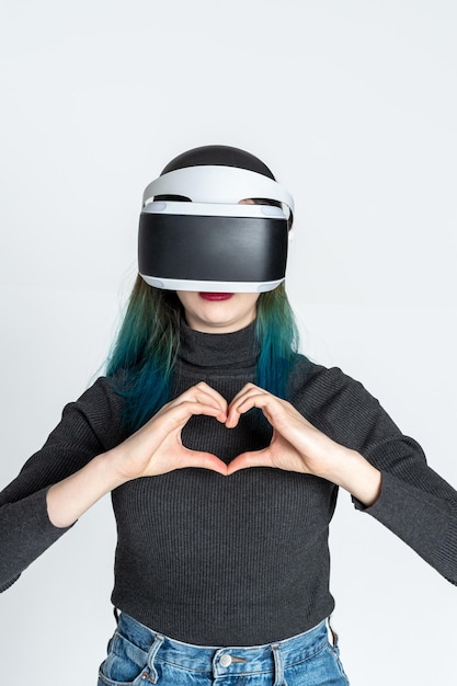 Teenie-Mädchen mit VR-Helm zeigt Herzgeste mit den Händen auf weißem Hintergrund Virtuelles Liebeskonzept Das Konzept des virtuellen sozialen Universums der Metaverse-Virtual-Reality