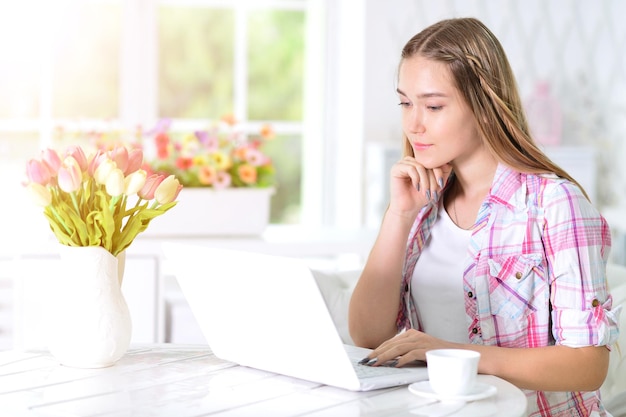 Teenie-Mädchen sitzt am Tisch und benutzt Laptop