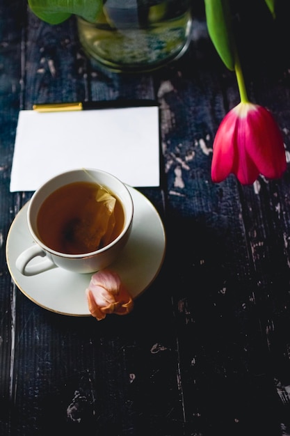 Teetasse auf hölzernem Hintergrund mit Frühlingstulpen und weißem Blatt