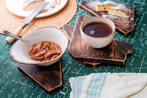 Teezeit, Aprikosenmarmelade, Hüttenkäsekuchen und Tasse Tee auf Holzbrettern, mathematische Formeln auf Tischdeckenhintergrund.