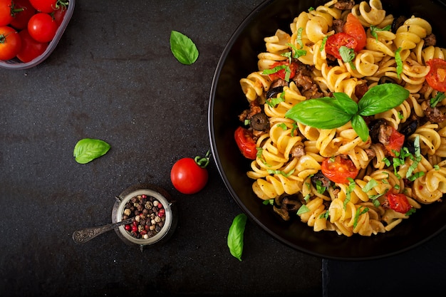 Teigwaren Fusilli mit Tomaten, Rindfleisch und Basilikum in der schwarzen Schüssel auf Tabelle.