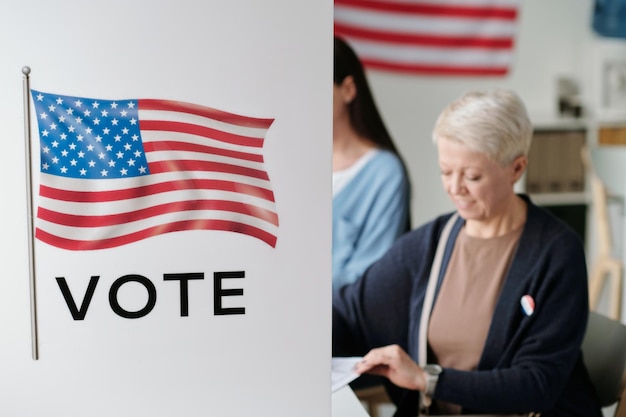 Foto teil der wahlkabine mit amerikanischer flagge und zwei dahinter sitzenden wählern