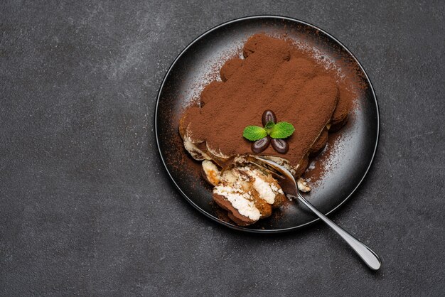 Teil des klassischen Tiramisu-Desserts auf Keramikplatte auf Betonhintergrund oder -tisch