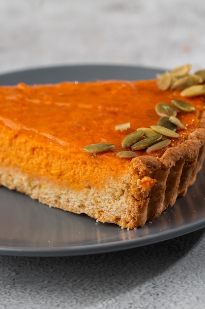 Teil des köstlichen offenen Kuchens der leuchtend orange Kürbis auf grauem Teller, verziert mit Kürbiskernen mit Dessertgabel-Nahaufnahme, Draufsicht. Heller Marmorhintergrund. Speicherplatz kopieren. Vertikale. Menü für Cafe