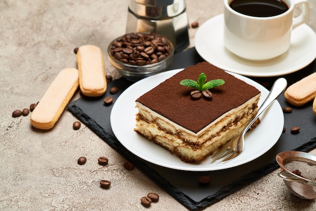 Foto teil des traditionellen italienischen tiramisu-desserts und der mokka-kaffeemaschine auf grauem betontisch