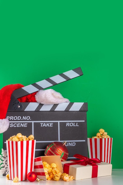 Teil des Weihnachtsfilmabends. Treffen Sie Freunde und Familie zum Heimkino. Einladungen zur Neujahrs-Weihnachtsfilmpremiere mit einer Filmklappe, einer Christbaumkugel, einem Eimer Popcorn und einer Weihnachtsmütze