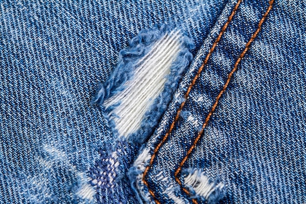 Teil einer blauen Denim-Jeans-Hintergrundtasche mit Schäden und Nähten mit orangefarbenen Fadenstichen