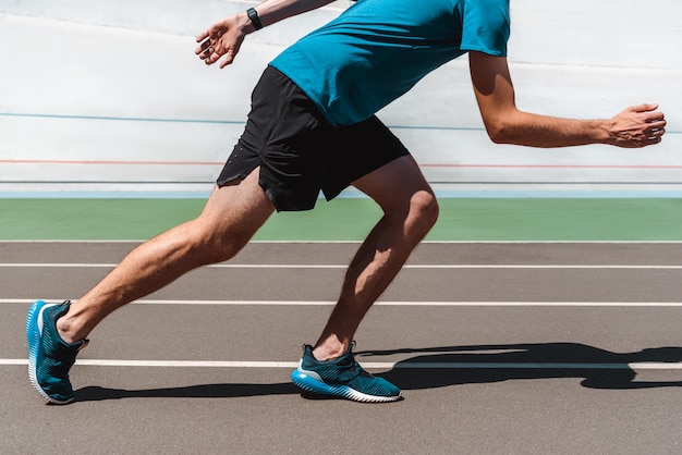 Foto teilansicht des sportlichen jungen sportlers, der auf laufbahn joggt