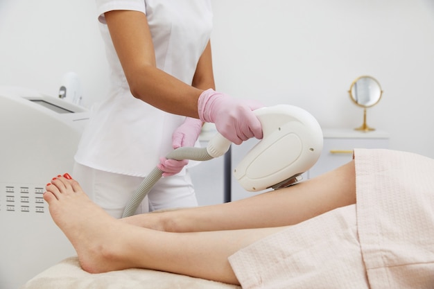 Teilansicht einer Frau, die in einem Salon eine Laser-Haarentfernung am Bein erhält