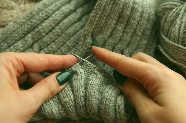 Tejer - manos de mujer joven con agujas de tejer y rollo de lana gris. mujer manos tejer bufanda