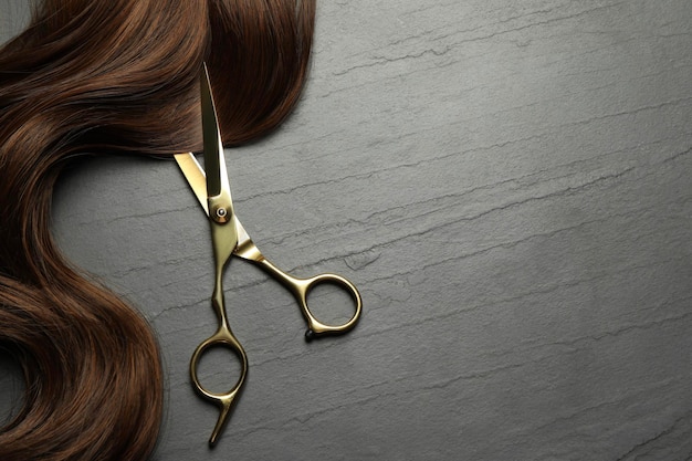 Tejeras de peluquería profesionales con hilo de cabello marrón en la vista superior de la mesa gris oscuro Espacio para el texto