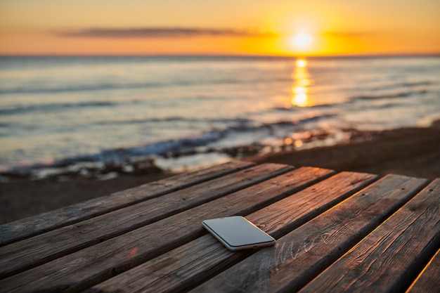 UN TELÉFONO SOBRE UNA MESA EN UNA PUESTA DE SOL EN LA PLAYA