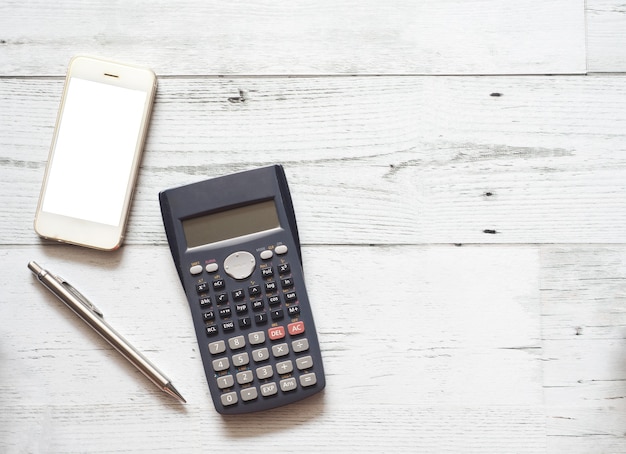 Tela branca do smartphone e caneta prateada e calculadora no conceito de negócio de mesa de madeira branca