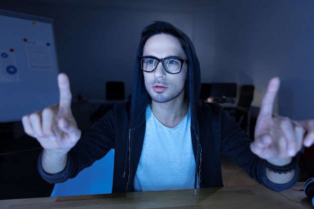 Tela sensorial. agradável homem barbudo sentado à mesa e olhando para os dedos enquanto trabalha na tela sensorial