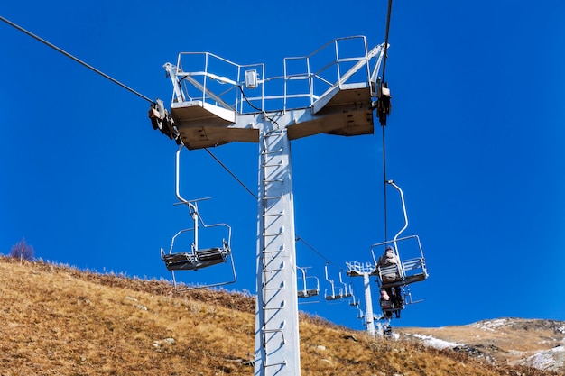 Teleférico com mecanismos de elevação nas montanhas em um dia claro de sol contra um céu azul. Recreação ativa e esportes de inverno.