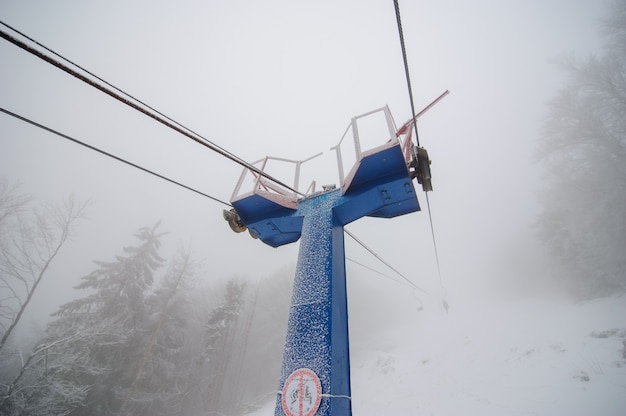 Teleférico hasta la montaña en el bosque de invierno. El bosque está cubierto de nieve. Clima nublado. Mala visibilidad