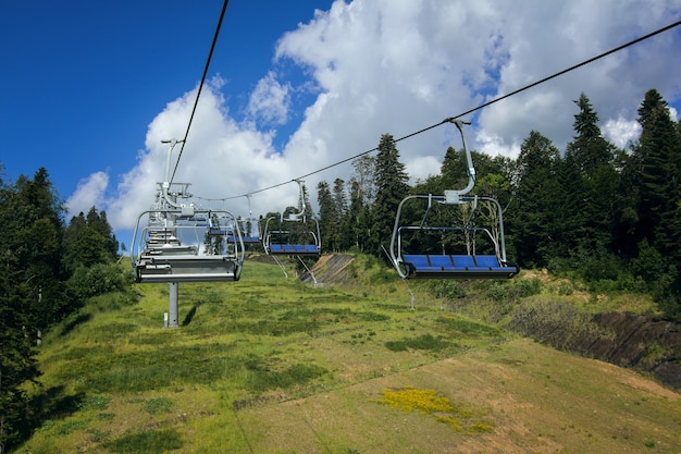 Teleférico sobre el bosque de montaña en un día de verano Bosques verdes colinas prados cubiertos de hierba y cielo azul