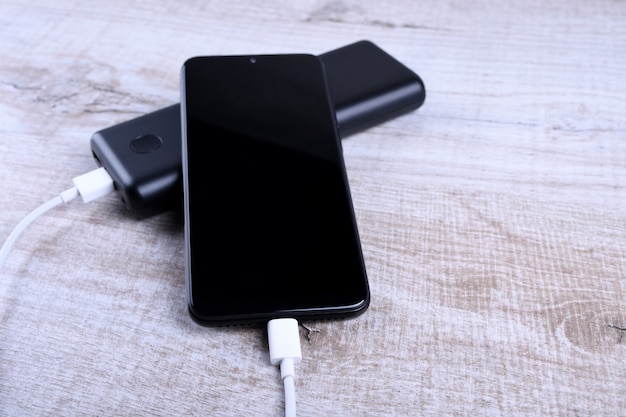 Telefon aufladen, Powerbank lädt Smartphone, Handy mit Energiebank. Schärfentiefe auf Power Bank auf Holztisch