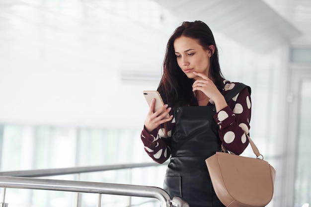 Telefon halten Schöne junge Brünette im schwarzen Rock drinnen im Büro oder Flughafen Freizeit haben